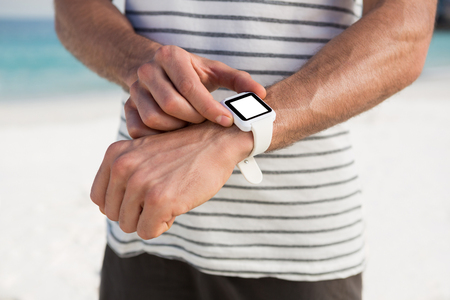 Midsection of man using smartwatch while standing at beachの写真素材