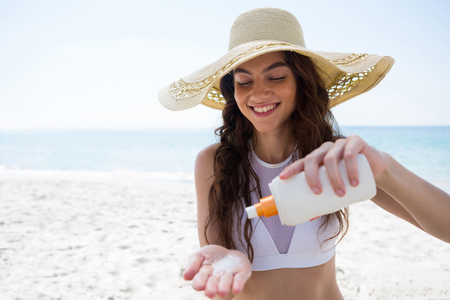 Smiling woman pouring cream on palm at beachの写真素材