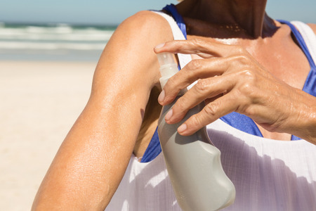 Cropped image of woman applying lotion while standing at beach on sunny day