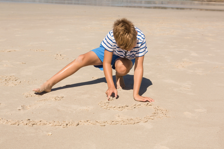 Boy playing with sand while crouching at beach on sunny dayの写真素材