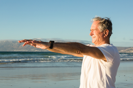 Close up of senior man exercising at beach against clear skyの写真素材