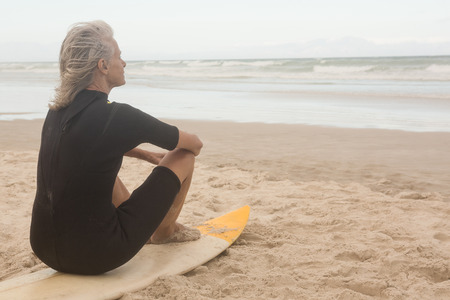 Rear view of senior woman sitting on surfboard at beach