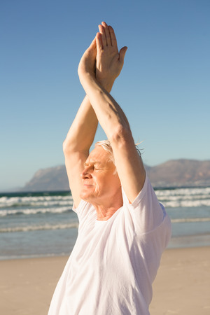 Senior man with eyes closed exercising at beach on sunny dayの写真素材