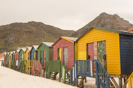 Multi colored wooden beach huts on sand against mountainの写真素材