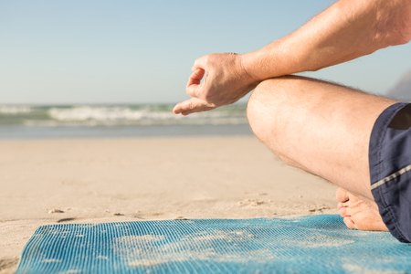 Cropped image of senior man meditating at beach on sunny dayの写真素材