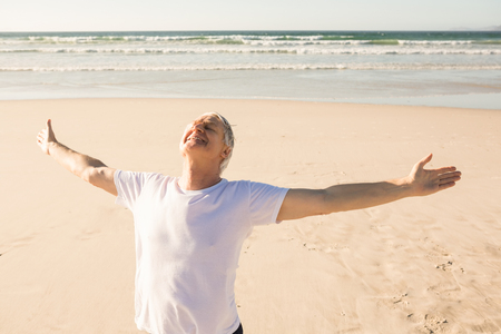 Active senior man with arms outstretched practicing yoga at beach on sunny dayの写真素材