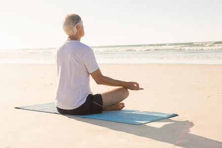 Senior man doing yoga at beach on sunny dayの写真素材
