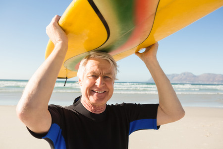 Portrait of senior man carrying surfboard at beach on sunny dayの写真素材