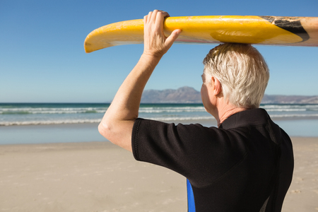 Senior man carrying surfboard on head at beach during sunny dayの写真素材
