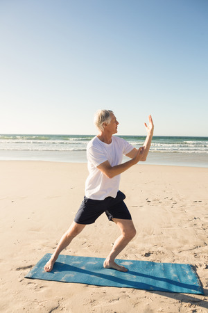 Full length of active senior man practicing yoga at beach during sunny dayの写真素材