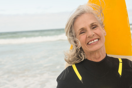 Close up of smiling woman with surfboard standing against sea at beach