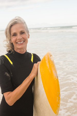 Portrait of smiling woman carrying surfboard while standing on shore at beachの写真素材