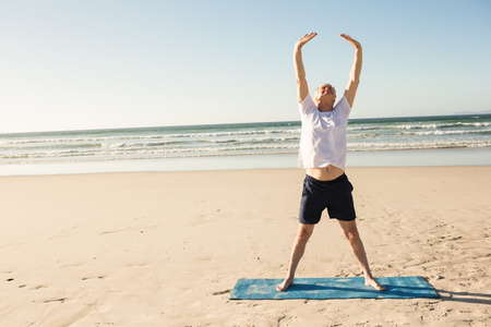 Full length of senior man stretching at beach on sunny dayの写真素材