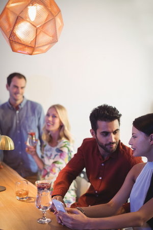 Couple interacting with each other while using mobile phone at bar counter in restaurantの写真素材