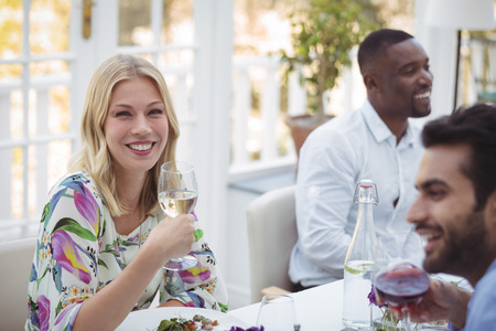 Portrait of smiling woman having wine during lunch in restaurantの写真素材