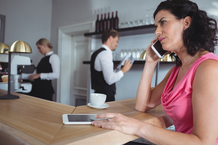 Woman sitting at bar counter talking on mobile phone in restaurantの写真素材
