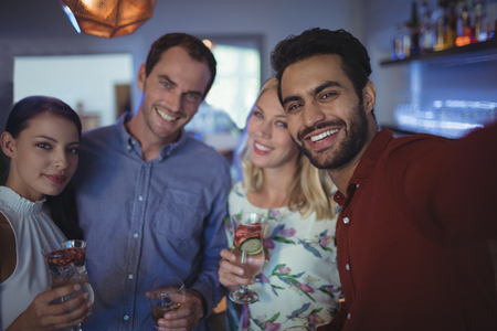Smiling two couples holding glasses of cocktail at bar restaurantの写真素材
