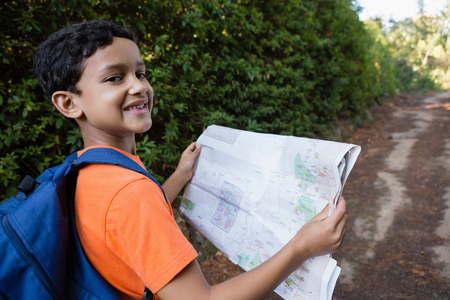 Smiling boy reading the map while walking on the path in forestの写真素材