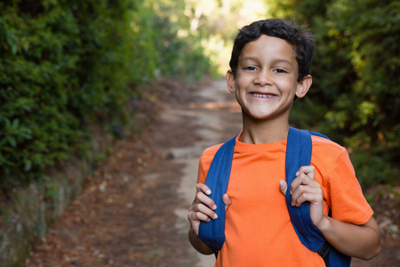 Portrait of smiling boy with backpack standing on the path in forest