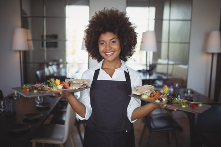Portrait of smiling waitress holding food tray in restaurantの写真素材