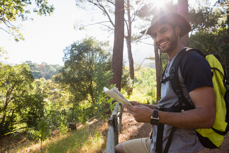 Smiling man holding the map and standing near the fence in forestの写真素材