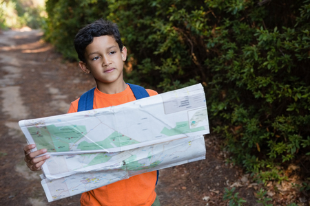 Boy holding the map and looking at the distance in the forestの写真素材
