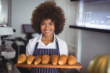 Portrait of smiling waitress holding croissants in wooden tray at restaurantの写真素材
