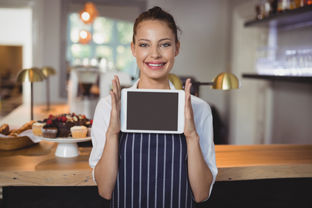 Portrait of waitress holding digital tablet at counter in restaurantの写真素材