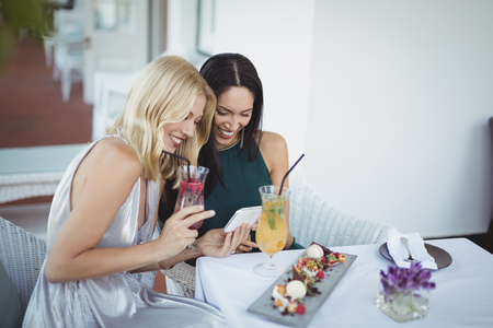 Smiling womens using mobile phone at restaurantの写真素材