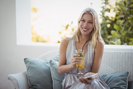 Portrait of woman holding cocktail glass and mobile phone at restaurantの写真素材