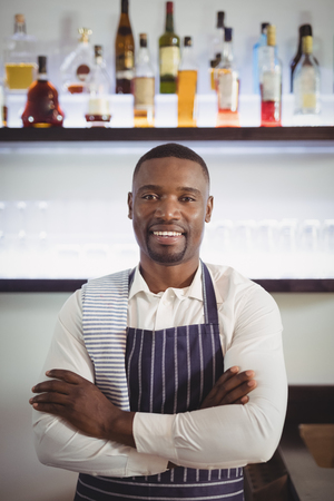 Portrait of smiling waiter standing with arms crossed at counter in restaurantの写真素材
