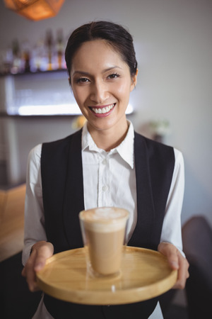 Portrait of waitress holding tray with glass of coffee in restaurant