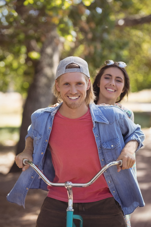 Portrait of smiling couple riding bicycle against trees at forestの写真素材