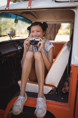 Cheerful woman holding camera while sitting in motor home at forestの写真素材