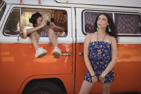 Woman photographing friend while sitting in van at forestの写真素材
