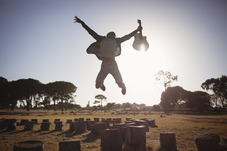 Happy man holding guitar while jumping against clear sky on sunny dayの写真素材