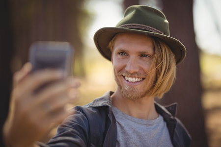 Close up of smiling young man clicking selfie while standing in forestの写真素材