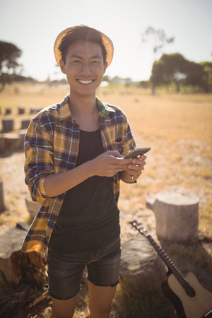 Portrait of smiling man using mobile phone while standing on fieldの写真素材