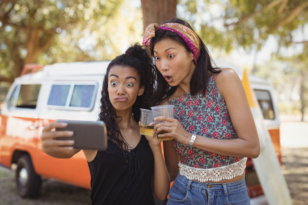 Young woman with friend taking selfie while standing by van on fieldの写真素材