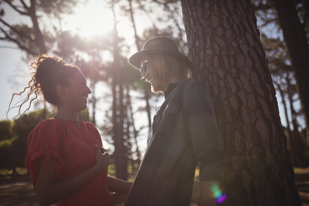 Low angle view of happy young couple looking at each other while standing together by tree trunk at forestの写真素材