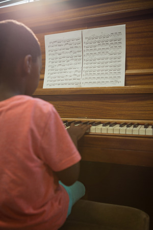 Rear view of boy practising piano in classroom at schoolの写真素材
