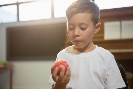 Close up of boy holding apple while standing against piano at homeの写真素材