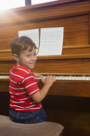 Portrait of smiling boy playing piano while sitting in classroom at schoolの写真素材