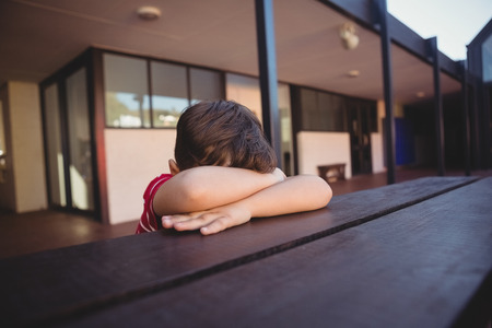 Close up of boy relaxing at table while sitting against school buildingの写真素材
