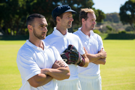 Confident cricket players standing at grassy field on sunny dayの写真素材