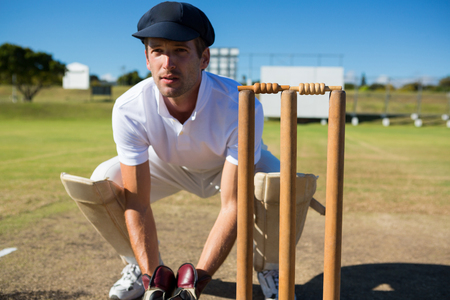 Wicket keeper crouching by stumps during match on sunny dayの写真素材