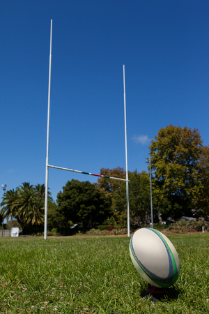 Low angle view of ball and rugby post on grassy field against clear blue skyの写真素材