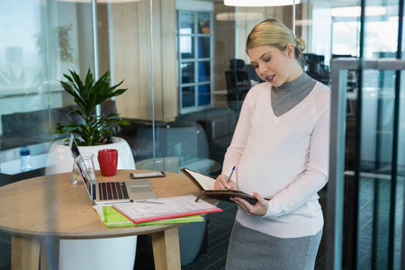 Pregnant businesswoman writing on a organizer at officeの写真素材