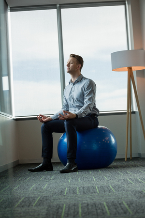 Executive meditating on fitness ball in officeの写真素材