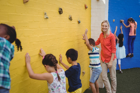 Trainer assisting kids in climbing wall in schoolの写真素材
